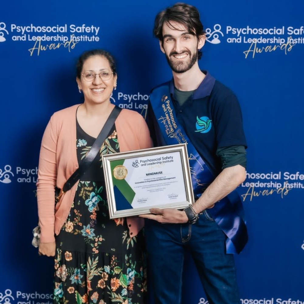 Two people smile while holding an award for innovation in psychosocial risk management.